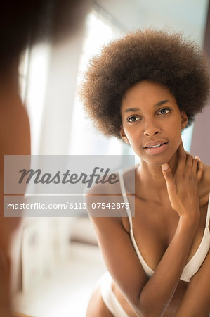 Woman in bra and panties examining herself in mirror