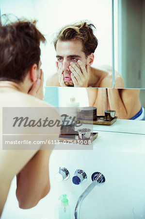 Hungover man examining himself in mirror