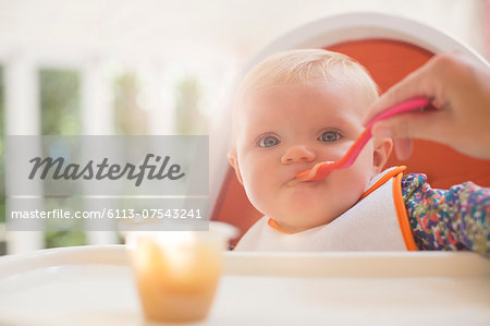 Mother feeding baby girl in high chair