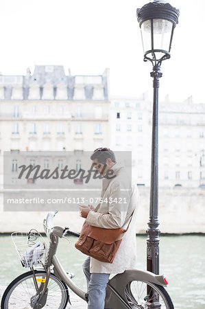 Businessman using cell phone on bicycle along Seine River, Paris, France