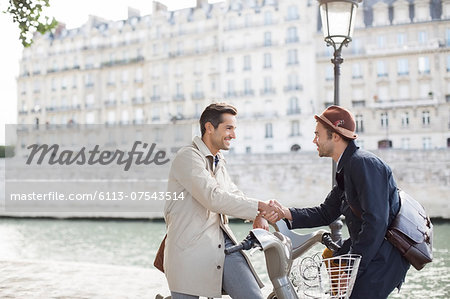 Businessmen handshaking on bicycles along Seine River, Paris, France Businessmen handshaking on bicycles along Seine River, Paris, France