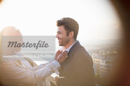 Woman holding boyfriend's collar on urban balcony