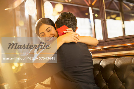 Woman with jewelry box hugging man in restaurant