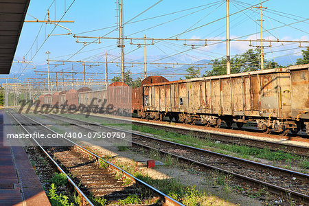 Old rusty freight cars stand on the track at the railway station.