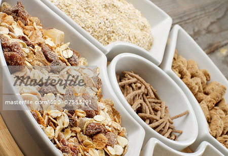 Muesli with Raisins and Nuts, Oat Flakes and Bran in White Plates closeup on Wooden background
