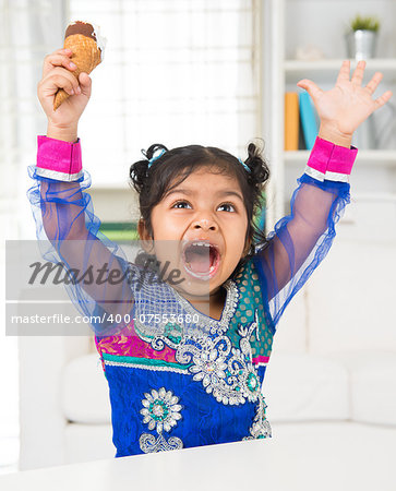 Eating ice cream. Cheerful Indian Asian girl enjoying an ice cream. Beautiful child model at home.