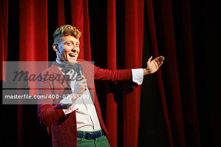 Arts and entertainment in theatre with funny man working as anchorman, standing against red curtains with microphone