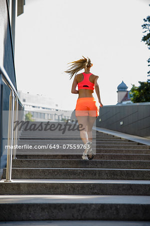 Young female runner moving up city stairway