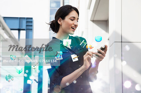 Young businesswoman holding smartphone with apps and icons coming out of it Young businesswoman holding smartphone with apps and icons coming out of it