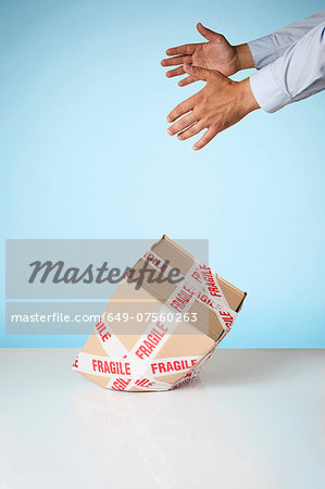 Studio shot of hands dropping cardboard box marked fragile Studio shot of hands dropping cardboard box marked fragile