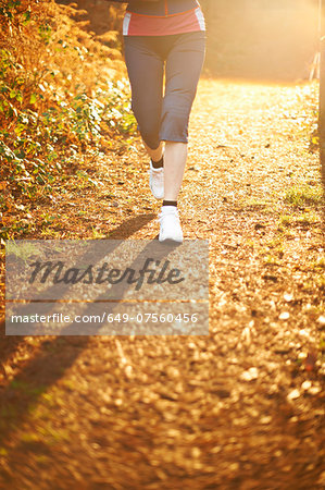 Mature woman jogging on path in sunlight, low section