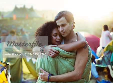 Couple in sleeping bag hugging outside tents at music festival