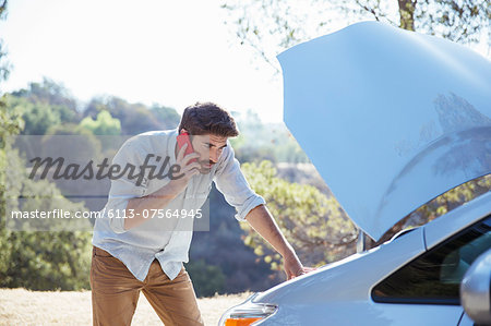 Man talking on cell phone and checking car engine at roadside