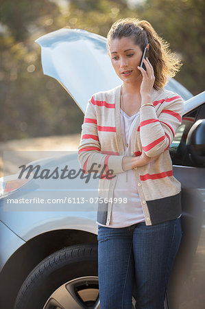 Woman talking on cell phone with automobile hood raised at roadside