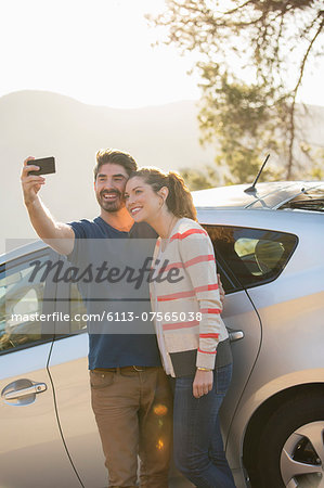 Couple taking self-portrait with camera phone outside car
