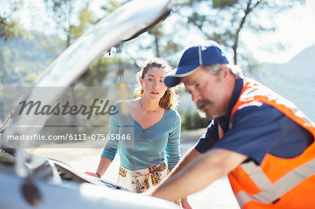 Woman watching roadside mechanic check car engine