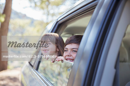 Happy brother and sister looking out car window