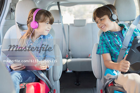 Happy brother and sister with headphones using digital tablets in back seat of car