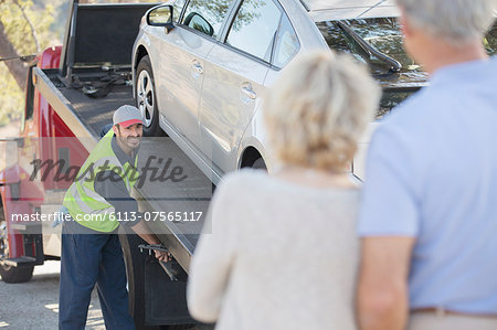 Senior couple watching roadside mechanic prepare to tow car