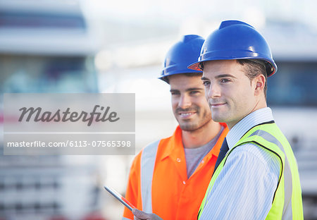 Businessman and worker using digital tablet near trucks