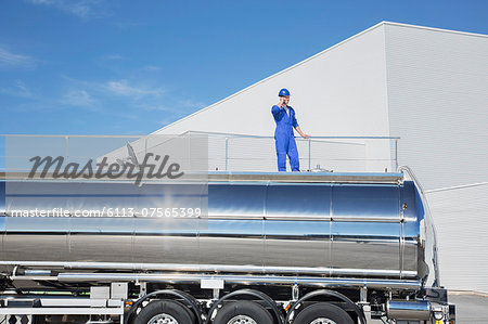 Worker talking on cell phone on platform above stainless steel milk tanker