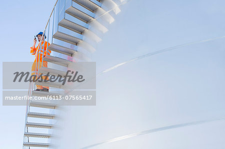 Worker using walkie-talkie on stairs along silage storage tower