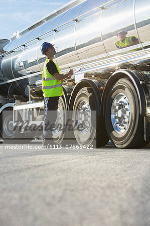 Worker with clipboard checking stainless steel milk tanker