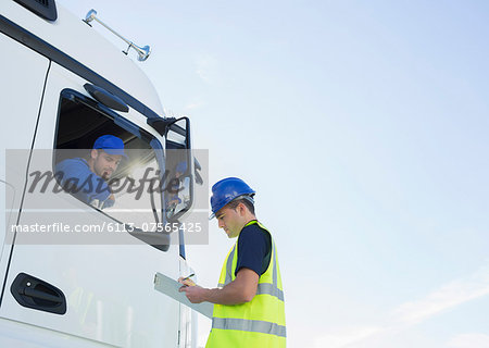 Worker with clipboard talking to truck driver