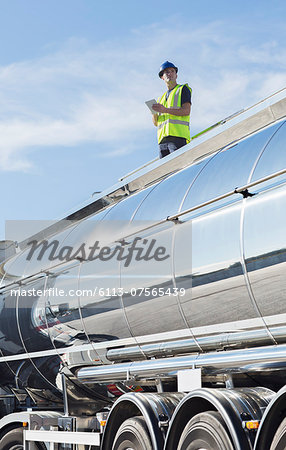Worker using digital tablet on platform above stainless steel milk tanker
