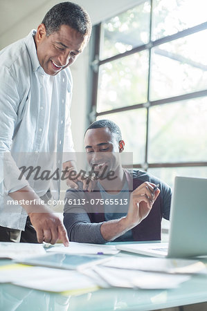 Father and son discussing paperwork at laptop Father and son discussing paperwork at laptop