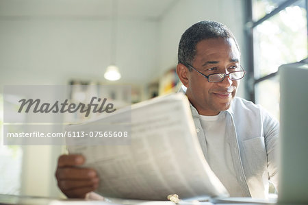 Senior man with newspaper using laptop