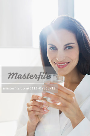 Portrait of smiling woman in bathrobe drinking water