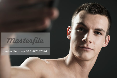 Close-up portrait of young man taking a selfie with cell phone, studio shot on black background