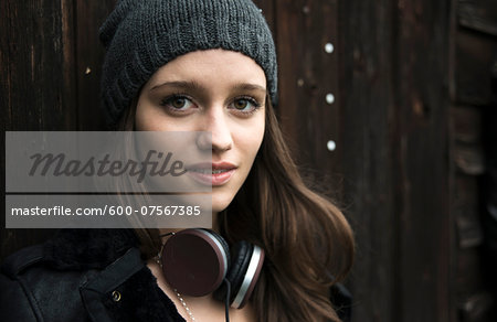 Close-up portrait of teenage girl outdoors, wearing hat and headphones around neck, looking at camera and smiling, Germany