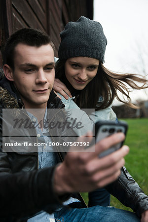 Close-up of young man and teenage girl outdoors, looking at cell phone, Germany