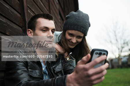 Close-up of young man and teenage girl outdoors, looking at cell phone, Germany