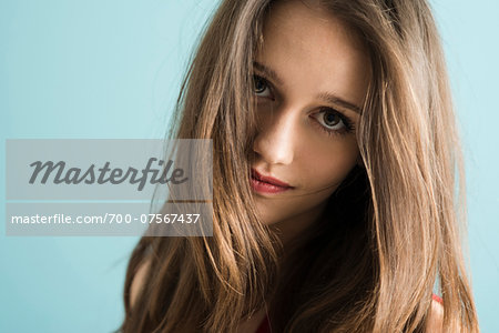 Close-up portrait of teenage girl looking at camera, studio shot on blue background
