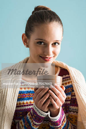Close-up portrait of teenage girl holding mug, looking at camera and smiling, studio shot on blue background