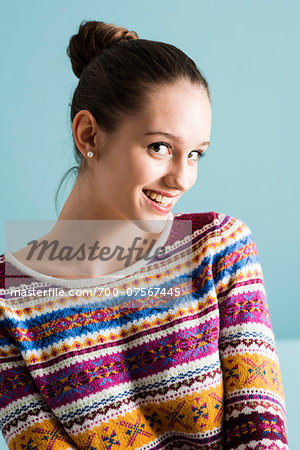 Close-up portrait of teenage girl with hair in bun, looking at camera and smiling, studio shot on blue background