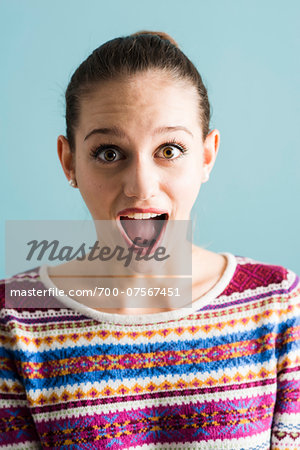 Close-up portrait of teenage girl, wide-eyed and with open mouth, studio shot on blue background