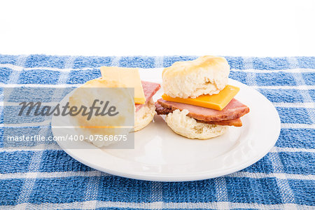Two ham and cheese biscuits on a white plate and blue towel with white background