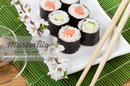 Japanese food and fresh sakura branch over bamboo table and mat