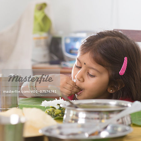 Indian family dining at home. Candid photo of Asian child self feeding rice with hand. India culture.