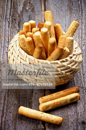Bunch of Bread Sticks with Sesame Seeds in Wicker Bowl on Rustic Wooden background