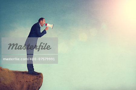 businessman shouting through a megaphone from a mountain edge