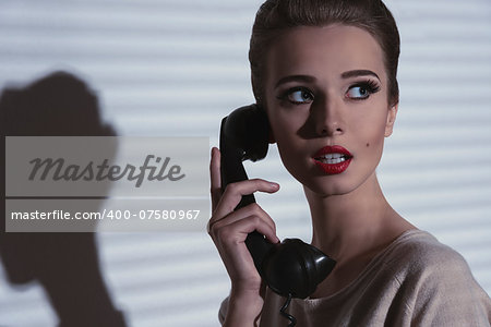 vintage woman with elegant hair-style and worried expression talking on the retro phone