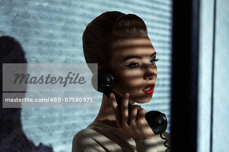 fashion shoot of vintage girl talking on phone with retro receiver in half-light atmosphere