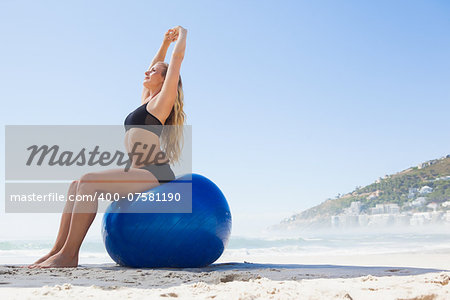 Fit blonde sitting on exercise ball at the beach on a sunny day