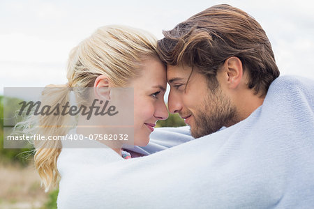 Cute affectionate couple standing outside wrapped in blanket on a chilly day
