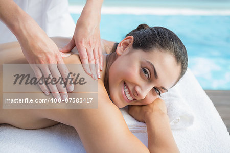 Smiling brunette getting a massage poolside looking at camera outside at the spa